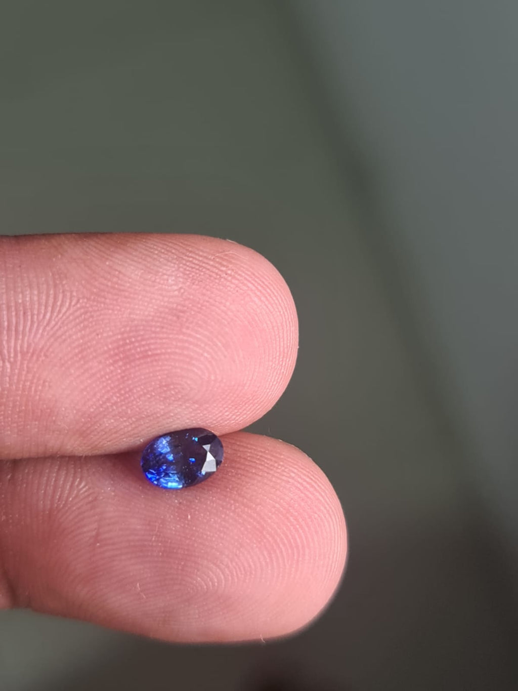 GS-000004 oval blue sapphire held between fingers — owner photograph